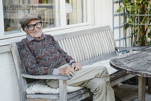 Lächelnder älterer Mann sitzt auf einer Bank im Hinterhof