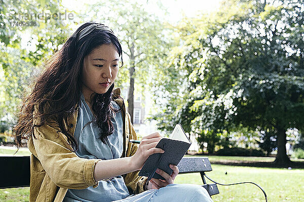 Junge Frau konzentriert sich  während sie im Park Tagebuch schreibt