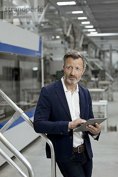 Männlicher Berufstätiger mit digitalem Tablet lehnt am Geländer in der Fabrik