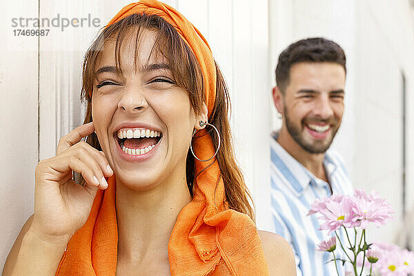 Frau lacht  während Mann mit Blumen im Hintergrund an der Wand steht
