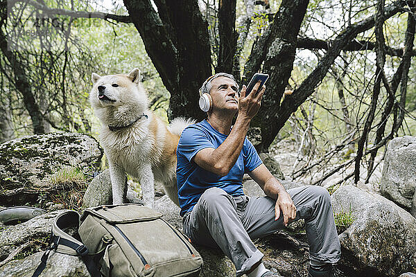 Mann nimmt Naturgeräusche per Smartphone auf  während er neben Hund im Wald sitzt