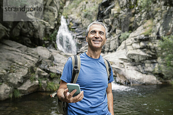 Lächelnder männlicher Tourist mit Mobiltelefon im Wald