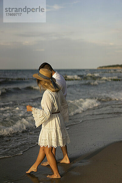 Freundin spaziert mit Freund am Strand bei Sonnenuntergang