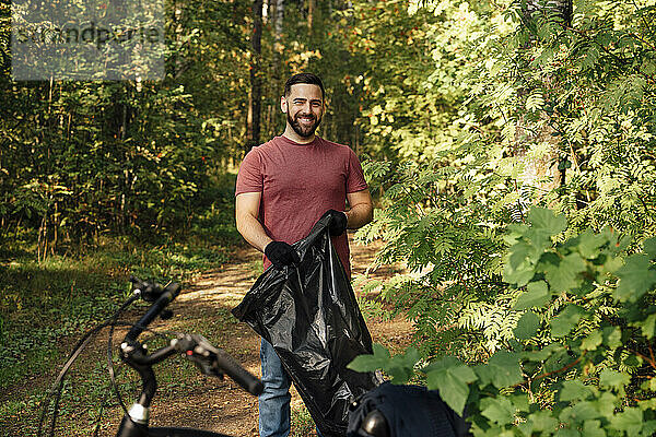 Lächelnder männlicher Freiwilliger hält Müllsack im Wald