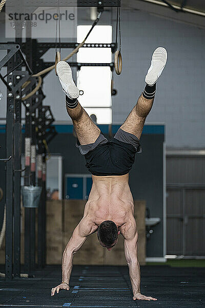 Nackter Oberkörper Sportler übt Handstand beim Training im Fitnessstudio