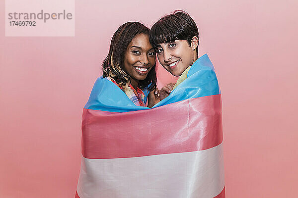 Lächelnde Freundinnen mit Transgender-Flagge vor rosa Hintergrund