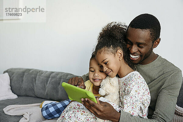 Glücklicher Vater mit Sohn und Tochter  die im Wohnzimmer ein digitales Tablet nutzen