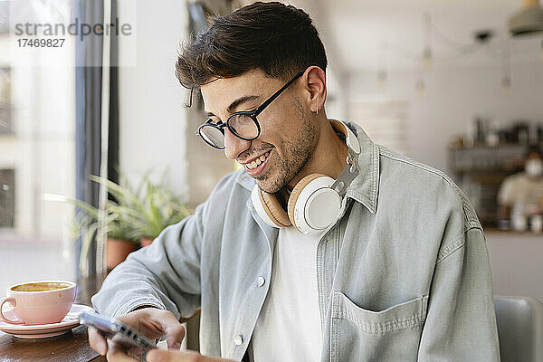 Lächelnder Geschäftsmann mit Brille benutzt Mobiltelefon im Café