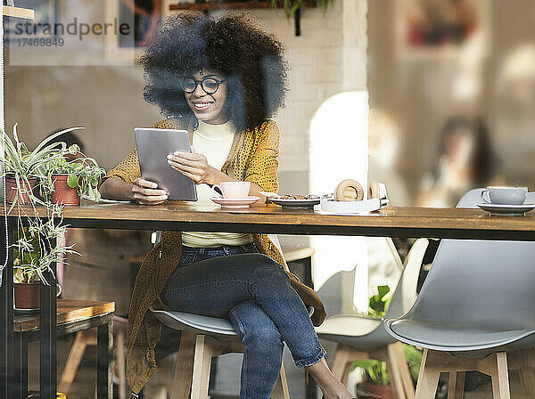 Lächelnde Frau mit Afro-Frisur mit Tablet-PC am Caféfenster