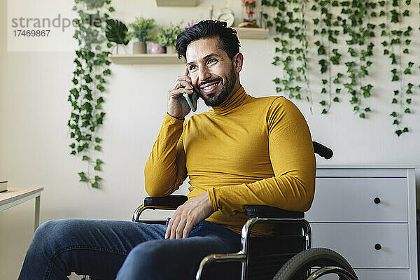 Lächelnder Mann mit Behinderung  der zu Hause mit dem Smartphone spricht
