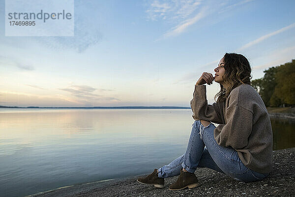 Nachdenkliche Frau sitzt auf einem Felsen und blickt auf den See
