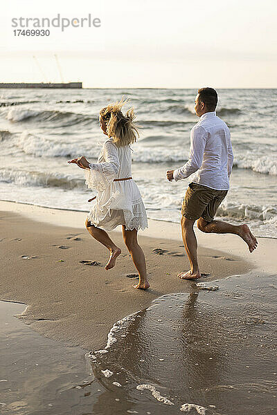 Verspieltes Paar läuft am Strand auf Sand am Meer