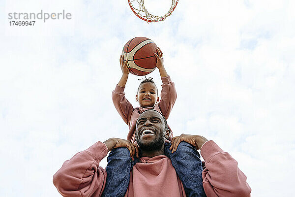 Fröhlicher Vater und Sohn spielen Basketball auf dem Sportplatz