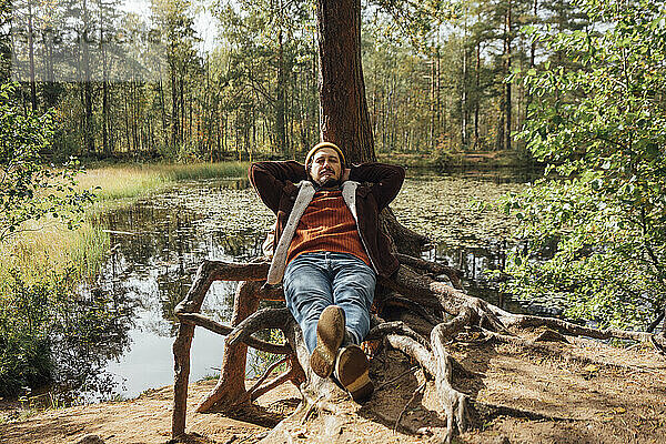 Mann mit geschlossenen Augen entspannt sich in der Nähe eines Baumes im Wald
