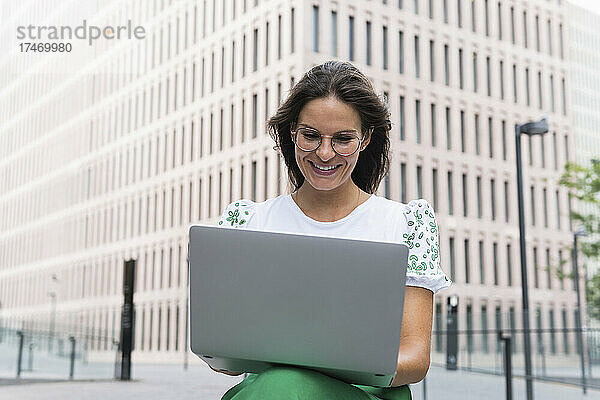 Lächelnde junge Geschäftsfrau  die in der Stadt am Laptop arbeitet