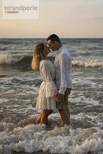 Paar reibt sich die Nase  während es bei Sonnenuntergang im Meer steht