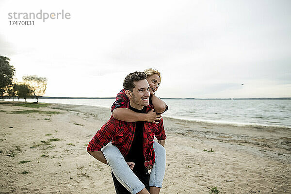 Lächelnder Freund gibt seiner Freundin Huckepackfahrt am Strand