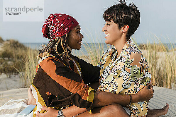 Lächelndes lesbisches Paar  das sich am Strand anschaut