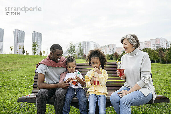 Vater blickt auf Kinder  die auf einer Parkbank etwas trinken