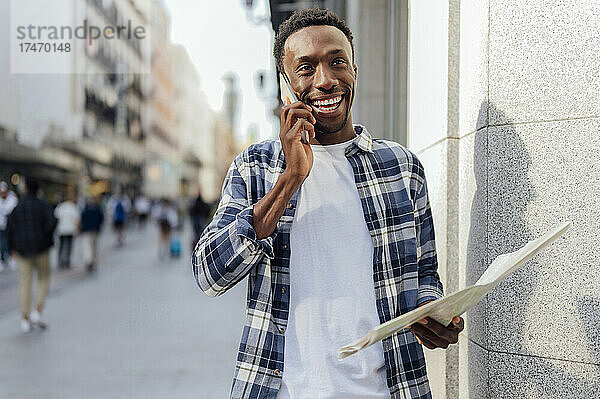 Lächelnder Tourist  der in der Stadt auf dem Smartphone spricht