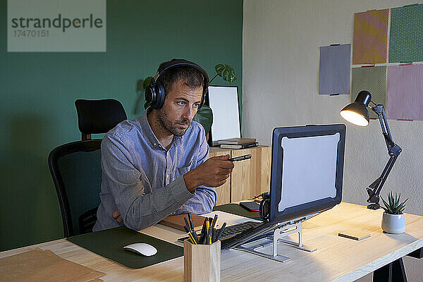 Geschäftsmann mit Kopfhörern zeigt im Heimbüro auf Laptop