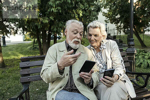 Paar benutzt Smartphones  während es auf Bank sitzt