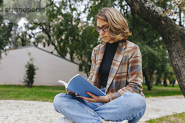 Geschäftsfrau sitzt mit gekreuzten Beinen und liest Buch im Park