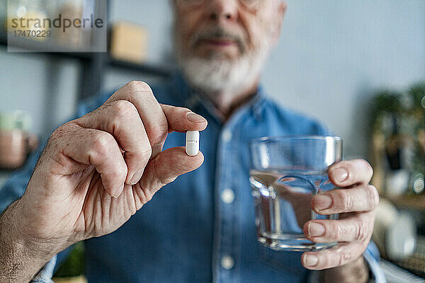 Älterer Mann hält ein Glas Wasser und eine Pille zu Hause