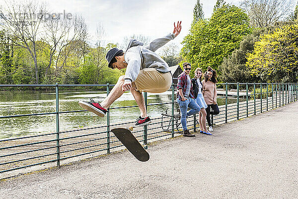Junger Mann zeigt Freunden im Park Stunt auf Skateboard