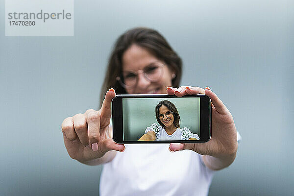 Lächelnde junge Frau  die mit dem Smartphone fotografiert