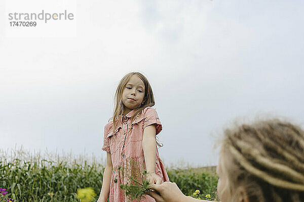 Mädchen hält Pflanze und schaut Mutter im Maisfeld an