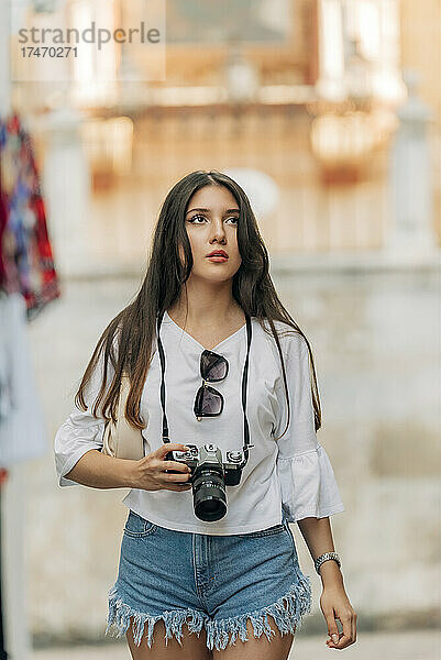 Junge Frau erwägt  eine Digitalkamera in der Hand zu halten