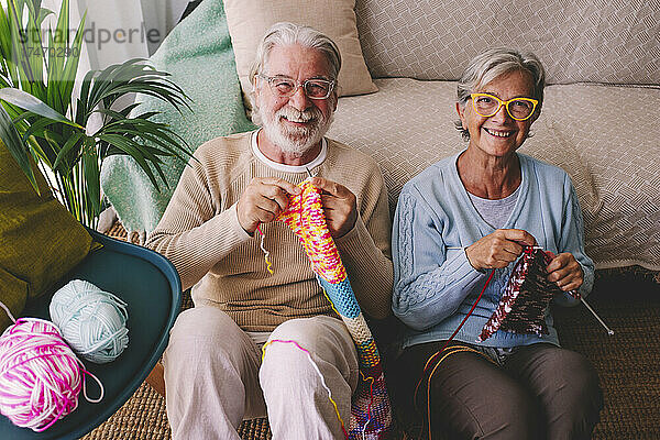 Lächelndes älteres Paar  das zu Hause Wolle strickt