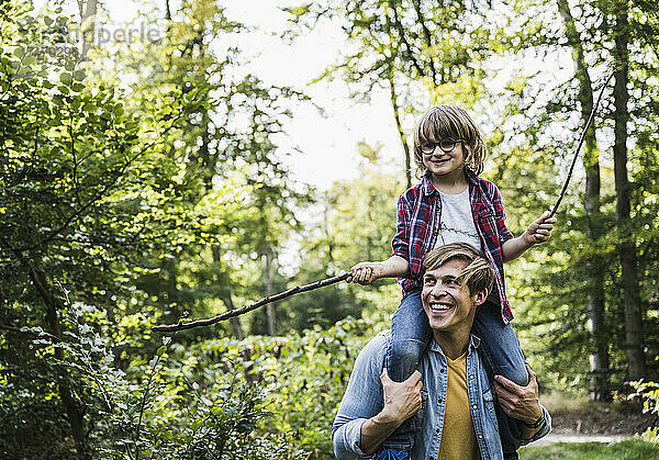 Glücklicher Vater trägt Sohn auf Schultern im Wald