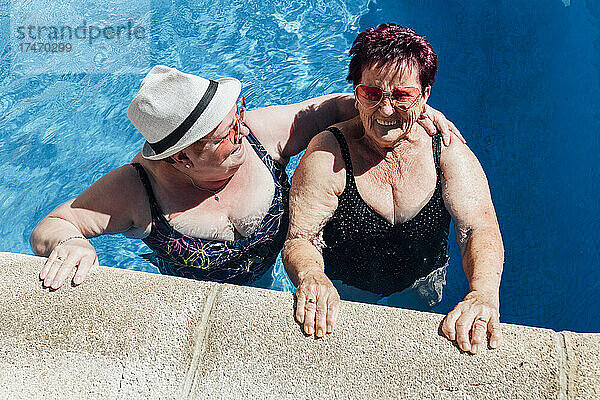 Glückliche Frau mit Hut spricht mit Freundin im Pool