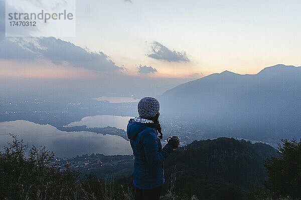 Junge Frau blickt bei Sonnenuntergang auf den Berg