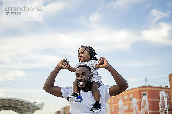 Glücklicher Mann trägt Tochter auf Schultern unter dem Himmel