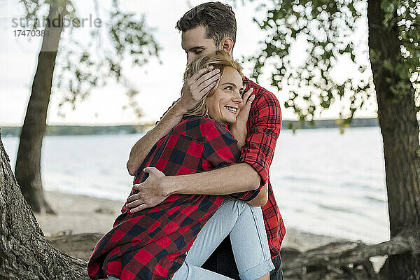 Junger Mann umarmt lächelnde Freundin am Strand