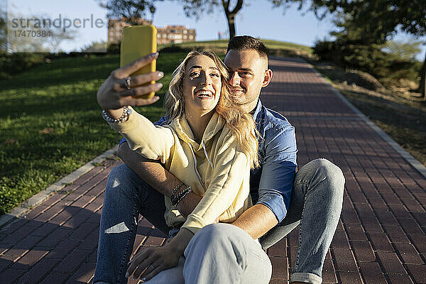 Lächelnde Freundin macht bei Sonnenuntergang ein Selfie mit ihrem Freund per Handy