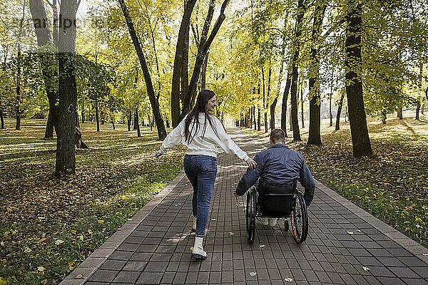 Verspielte Freundin läuft mit Freund im Rollstuhl im Park