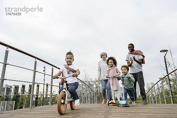 Vater jubelt den Kindern zu  die auf der Brücke Tretroller und Fahrrad fahren