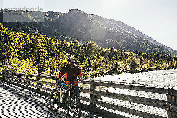 Lächelnder Mann fährt Mountainbike auf Brücke