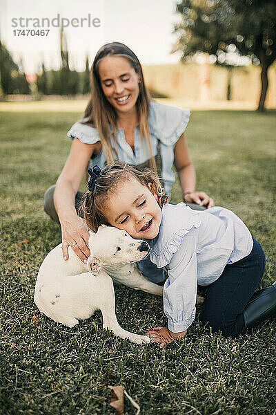 Glückliche Tochter spielt mit Hund  während Mutter im Hintergrund auf der Ranch steht