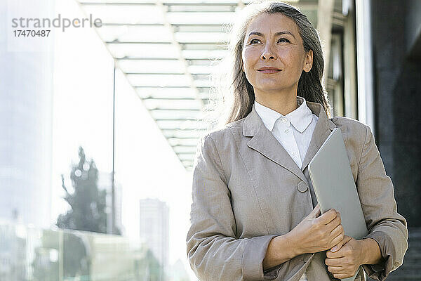 Lächelnde Geschäftsfrau mit grauem Haar  die einen Laptop hält