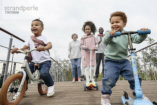 Glückliche Kinder spielen mit Tretrollern und Fahrrädern auf der Brücke