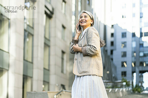 Reife Frau lächelt  während sie in der Stadt mit dem Smartphone spricht