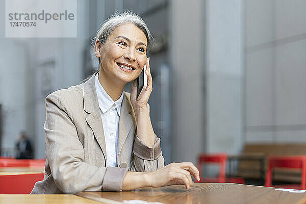 Reife Frau lächelt  während sie im Straßencafé mit dem Handy telefoniert