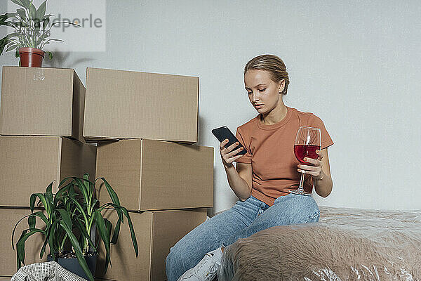Frau mit Weinglas benutzt Mobiltelefon in umgezogener Wohnung