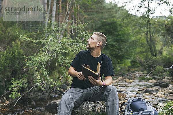 Mann mit Tagebuch sitzt auf Felsen im Wald