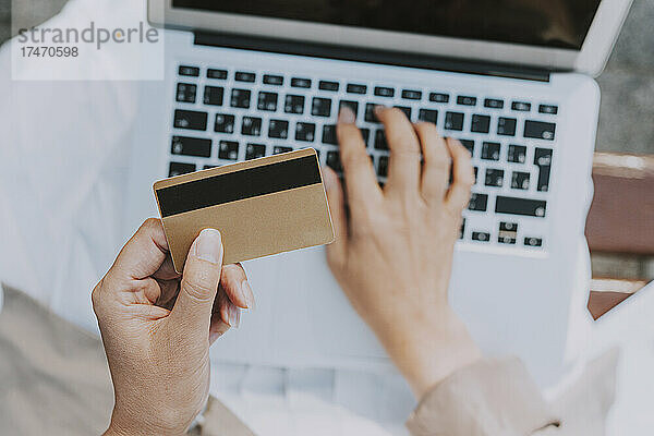 Reife Frau hält Kreditkarte in der Hand  während sie Laptop benutzt